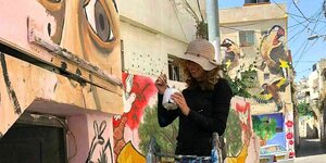 Laura Rosner steht auf einer Leiter und malt Augen auf eine Wand
