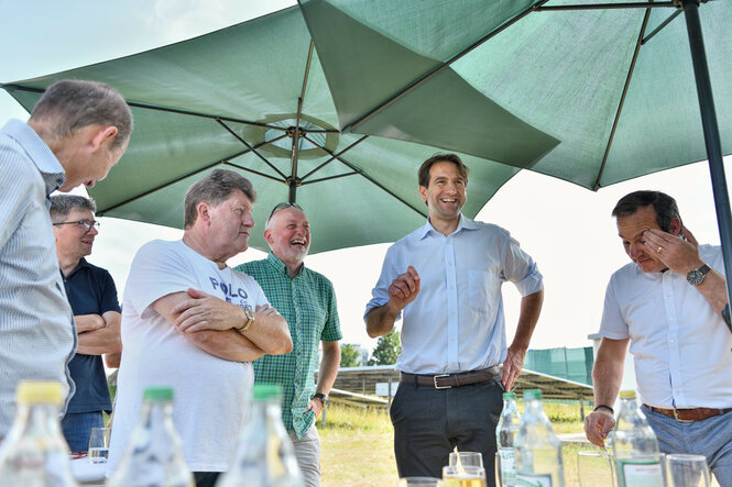 Andreas Jung steht unter Sonnenschirmen und spricht zu den Mitgliedern und lacht