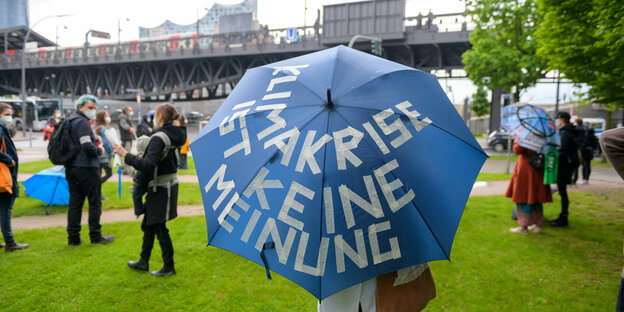 bei einer Demonstration trägt eine Person einen Regenschirm mit der Aufschrift: "Klimakrise ist keine Meinung"
