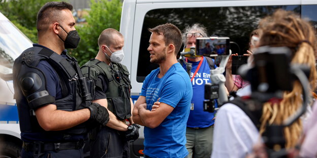Ein Demonstrant in blauem Hemd ohne Mund-Nasen-Maske spricht mit einem Polizeisten