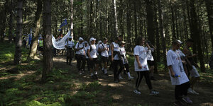 Eine Gruppe von Menschen läuft in einer Reihe durch einen schattigen Sommerwald