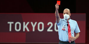 Ein Mann zeigt eine rote Karte mit der Aufschrift "Tokyo 2020"