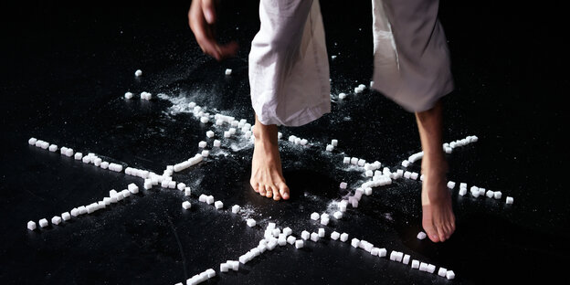 Zwei Füße tanzen durch Quadrate, die aus Zuckerwürfeln bestehen und auf dem Boden verteilt sind