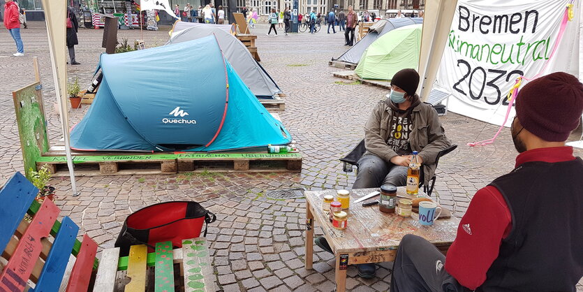 Aktivisten tobias und simon sitzen auf palettenmöbeln vor den zelten des klimacamps vor dem bremer rathaus