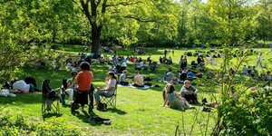 Zahlreiche Menschen genießen das Wetter bei strahlenden Sonnenschein in einem grünen Park