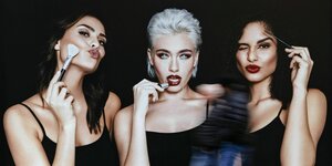 Drei extrem gestylte, schlanke junge Frauen schminken sich auf einem Plakat
