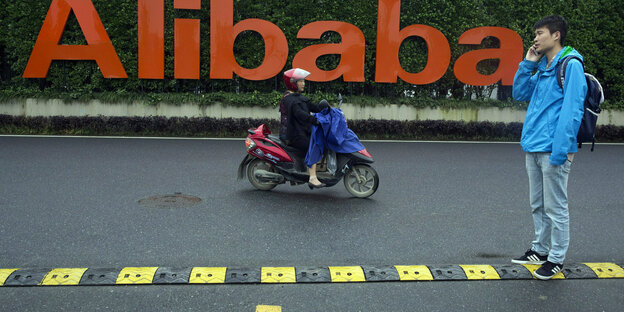 Ein mann mit Telefon und ein Moped vor einem Schriftzug.