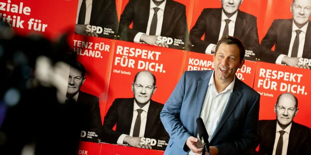 Ein Mann im Anzug vor einer Wand roter SPD Plakate mit Olaf Scholz darauf