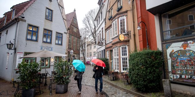 Zwei Menschen mit Regenschirm gehen durch das verregnete Schnoor, ein historisches Bremer Wohn- und Geschäftsviertel mit alten Häusern und besonders engen Gassen.