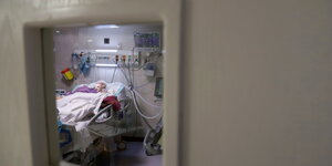 Ein/e Patient*in in einem Krankenbett ist durch ein Fenster zu sehen.