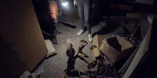 Ledergurte liegen auf dunklem Boden, angestrahlt mit einer Taschenlampe