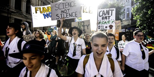Streikende Schüler und Schülerinnen in Uniform in Brisbane auf der Straße. Sie halten Schilder hoch auch denen gegen Ölförderung protestiert wird und mit "Science not Silence"