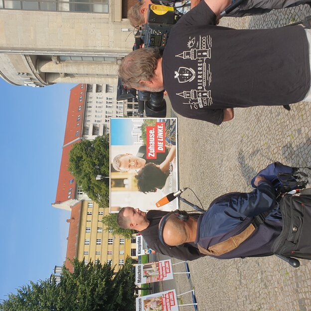 Klaus Lederer wird von mehreren Fernsehteams interviewt, dahiner das Plakat