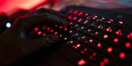 Ein Mann trägt Handschuhe und tippt auf einer Tastatur, deren Buchstaben rot leuchten