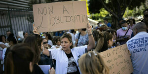 Eine Frau mit weissem Kittel hält ein Protestschild in die Höhe