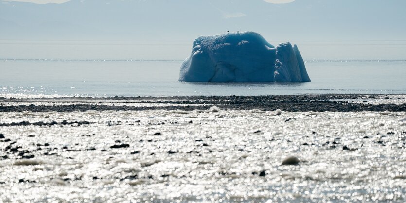 Ein Eisberg im Meer, im Hintergrund Berge