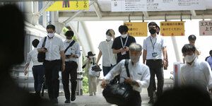 Japaner mit Gesichtsmasken gehen über eine Kreuzung