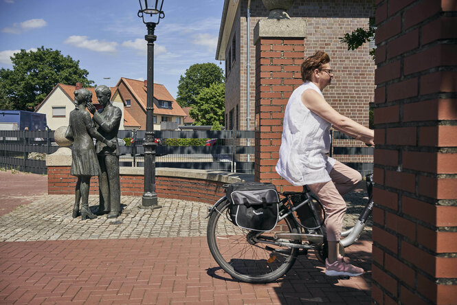 Eine Frau radelt an einer Statue von Lili Marleen vorbei