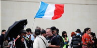 Ein Demonstrant mit Schirm hält eine französische Flagge in den Wind, umringt von Demonstranten