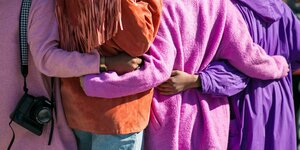 vier Menschen in lila Mänteln umarmen sich am Rücken
