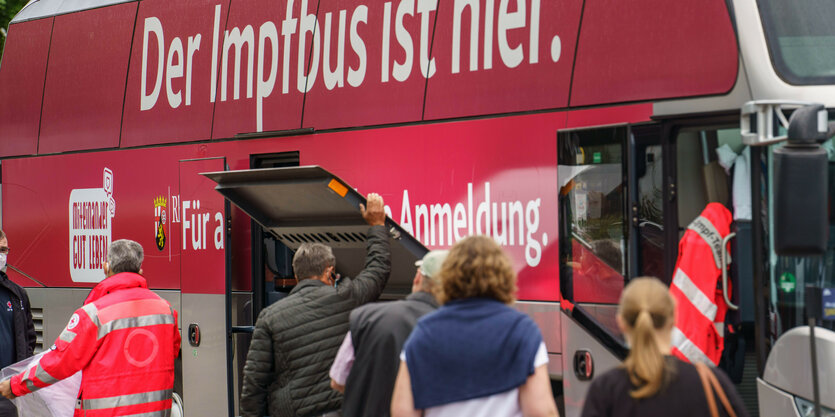 Menschen stehen vor einem roten Imfpbus Schlange