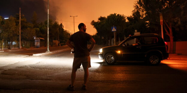 Ein Mann steht auf einer Straße, am Horizont Flammen und Rauch.
