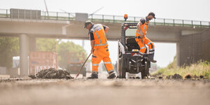 Zwei Bauarbeiter entfernen auf einer Autobahn Fugenmaterial aus der Fahrbahn