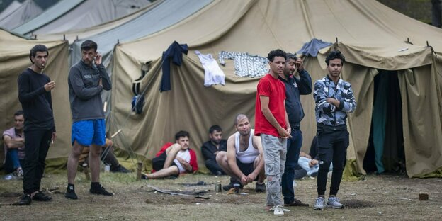 04.08.2021, Litauen, Rudninkai: Geflüchtete stehen vor Zelten auf dem Gelände des neu errichteten Flüchtlingslagers auf dem Truppenübungsplatz Rudninkai, etwa 38 km südlich von Vilnius.
