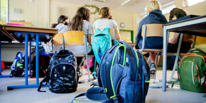 Schulranzen stehen in einem Klassenzimmer, in dem auch Kinder sitzen