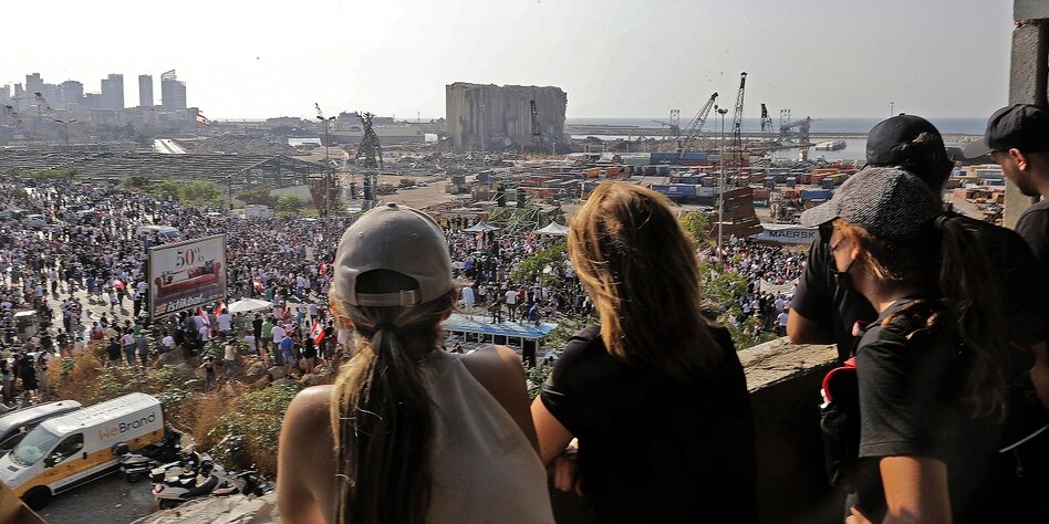 Junge Menschen schauen auf eine zerstörte Lagerhalle am Hafen von Beirut