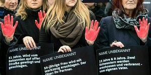 Frauen tragen Plakate mit den Namen von Todesopfern durch Femizide, die Hände der Demonstrantinnen sind mit roter Farbe bemalt