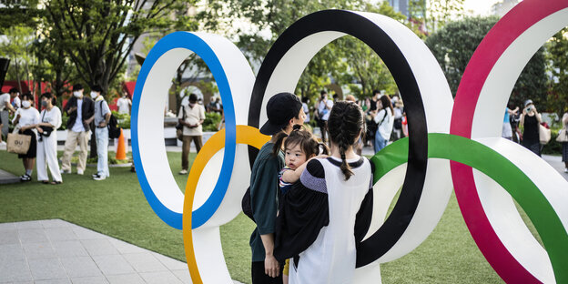 Junges Paar mit Kleinkind macht ein Foto mit den Olympischen Ringen vor dem Olympiastadion