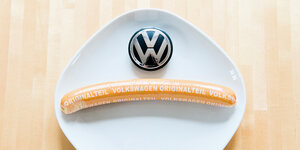 Zwei Würste mit der Aufschrift Volkswagen Originalteil über Kreuz, links oben das VW-Logo