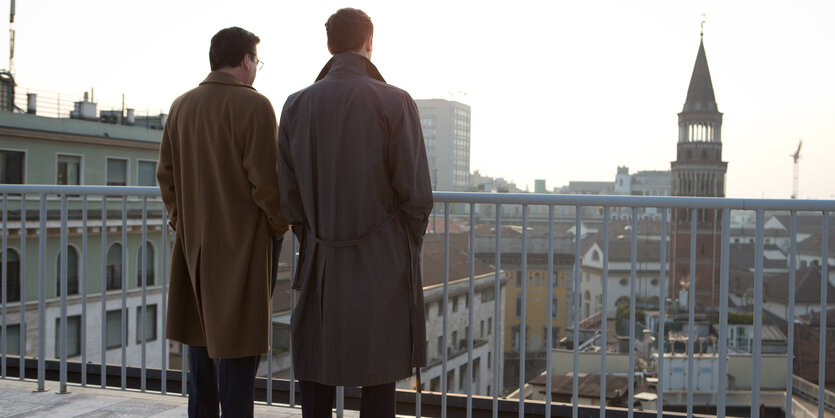 Zwei Männer stehen auf einer Brücke und schauen auf Häuser