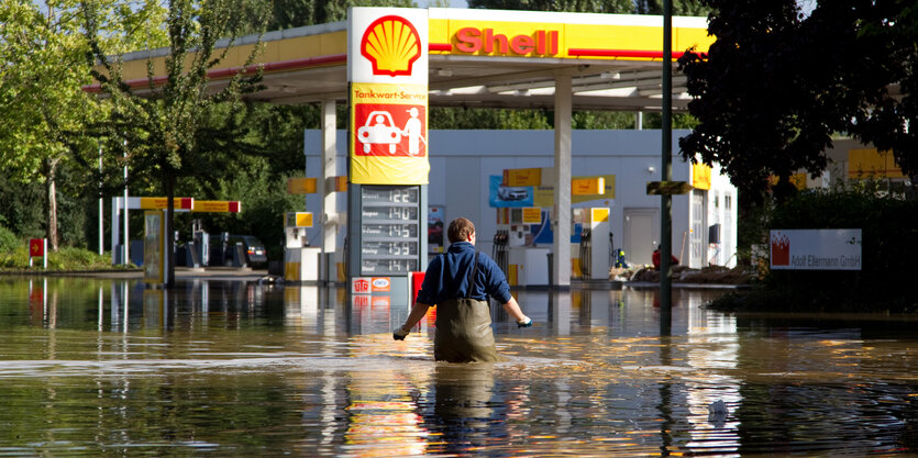 Ein Mann watet durch knietiefes Wasser auf eine Tankstelle zu