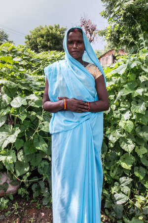 Eine Frau in blauem Sari steht vor einem Gebüsch