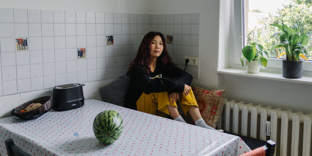 Eine junge Frau sitzt auf einer Bank an einem Küchentisch, auf dem eine Wassermelone liegt