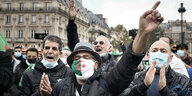 mehrer Männer demonstrieren, einer trägt eine Maske mit der algerischen Flagge