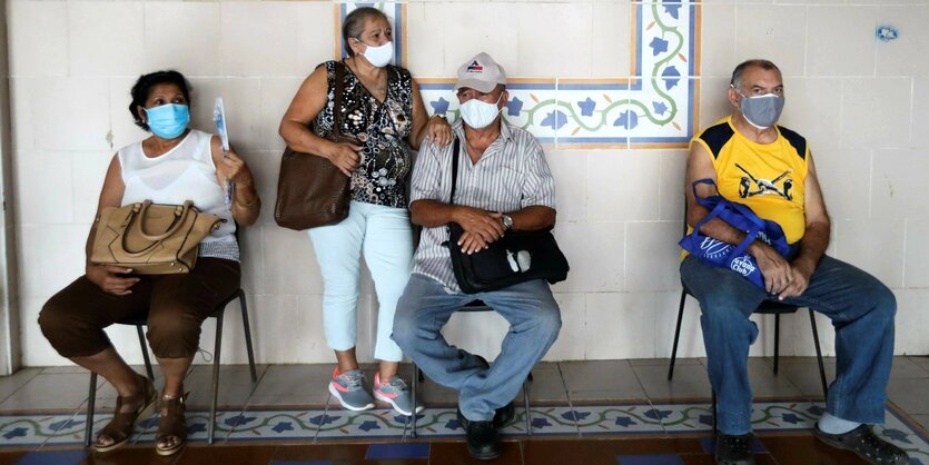 Zwei Männer und zwei Frauen auf Stühlen mit Gesichtsmasken warten