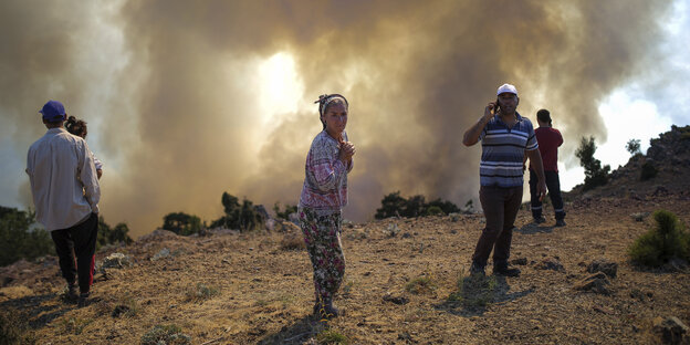 Menschen beobachten die Löscharbeiten eines Waldbrandes in Koycegiz