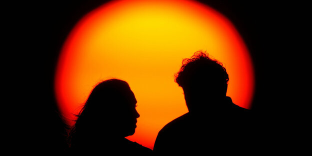 Zwei Personen stehen vor einer untergehenden Sonne