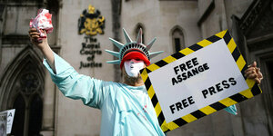 Ein Mann verkleidet als US-Freiheitsstatue hält ein Schild in der Hand: "Free Assange"