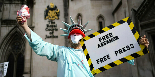 Ein Mann verkleidet als US-Freiheitsstatue hält ein Schild in der Hand: "Free Assange"