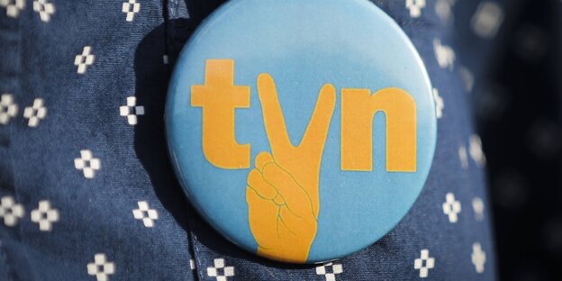 Ein Button mit dem Schriftzug des SEnders TVN und einer Hand, die das Victory-Zeichen macht