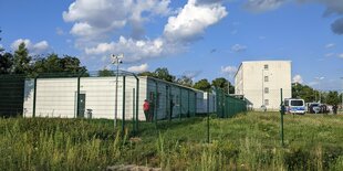 Links ein Container, rechts ein vierstöckiges Gebäude mti einem Polizeitransporter davor: Das Abschiebegefängnis am Berliner Flughafen.