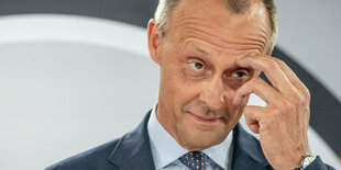 Friedrich Merz, ein alter Mann mit kurzen Haaren und großen Geheimratsecken. Er kratzt sich an der Augenbraue.