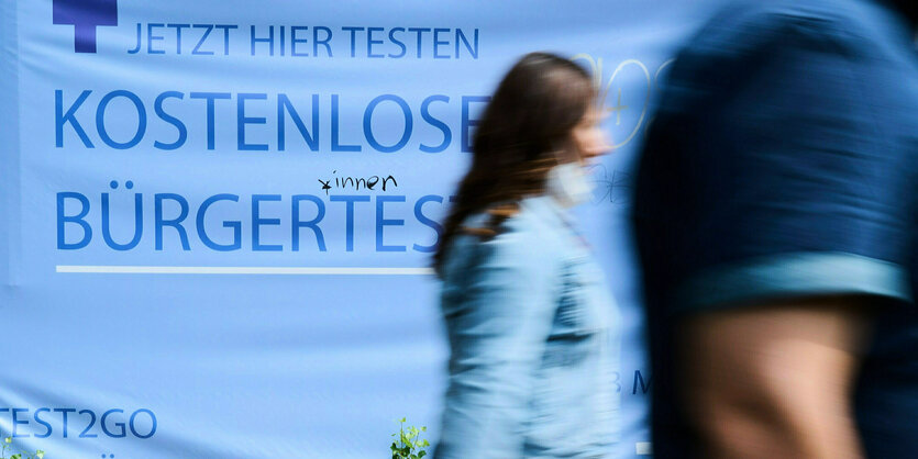 «Kostenlose Bürgertests» steht auf einem Plakat während Personen vorüber gehen