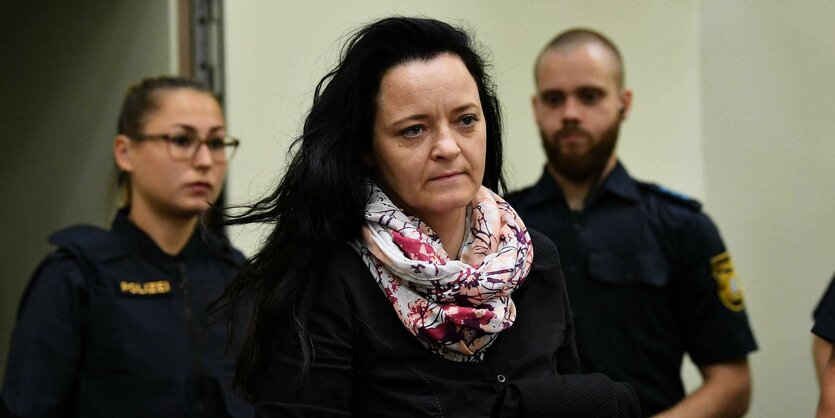 Beate Zschäpe im Gerictssaal, im Hintergrund unscharf zwei PolizistInnen