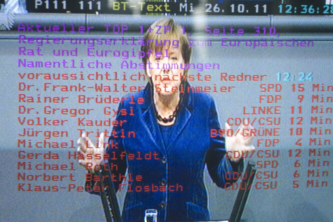 Merkel hält eine Rede, darüber liegt Text, gesehen durch einen Fernseher im Bundestag