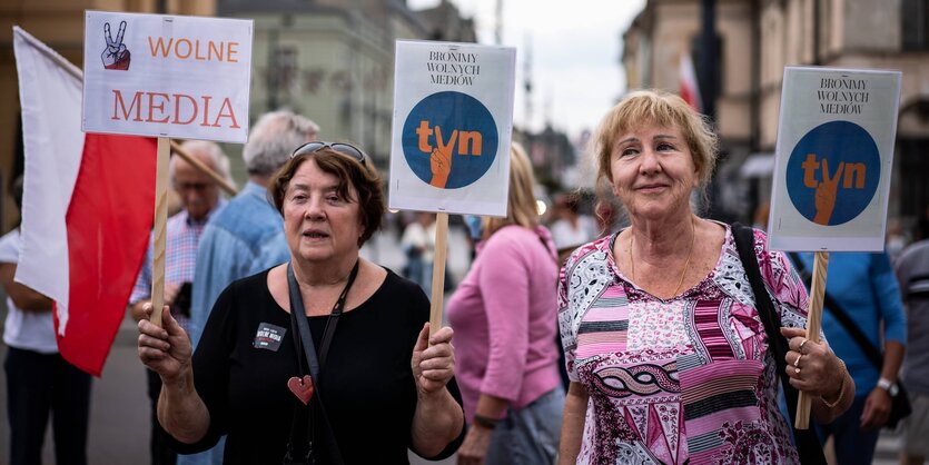 Zwei Frauen um die 60 auf einer Demonstration halten Schilder hoch, hinter ihnen weht eine Polen-Flagge